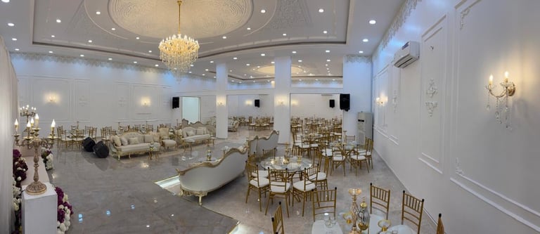 Elegant empty wedding banquet hall with white walls, crystal chandelier, gold chairs, and polished floor