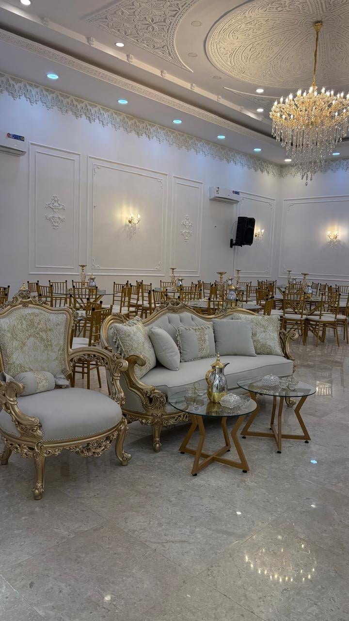 Elegant ballroom with ornate white paneled walls, crystal chandelier, and gilded Louis XVI-style furniture arrangement with blue upholstered seating