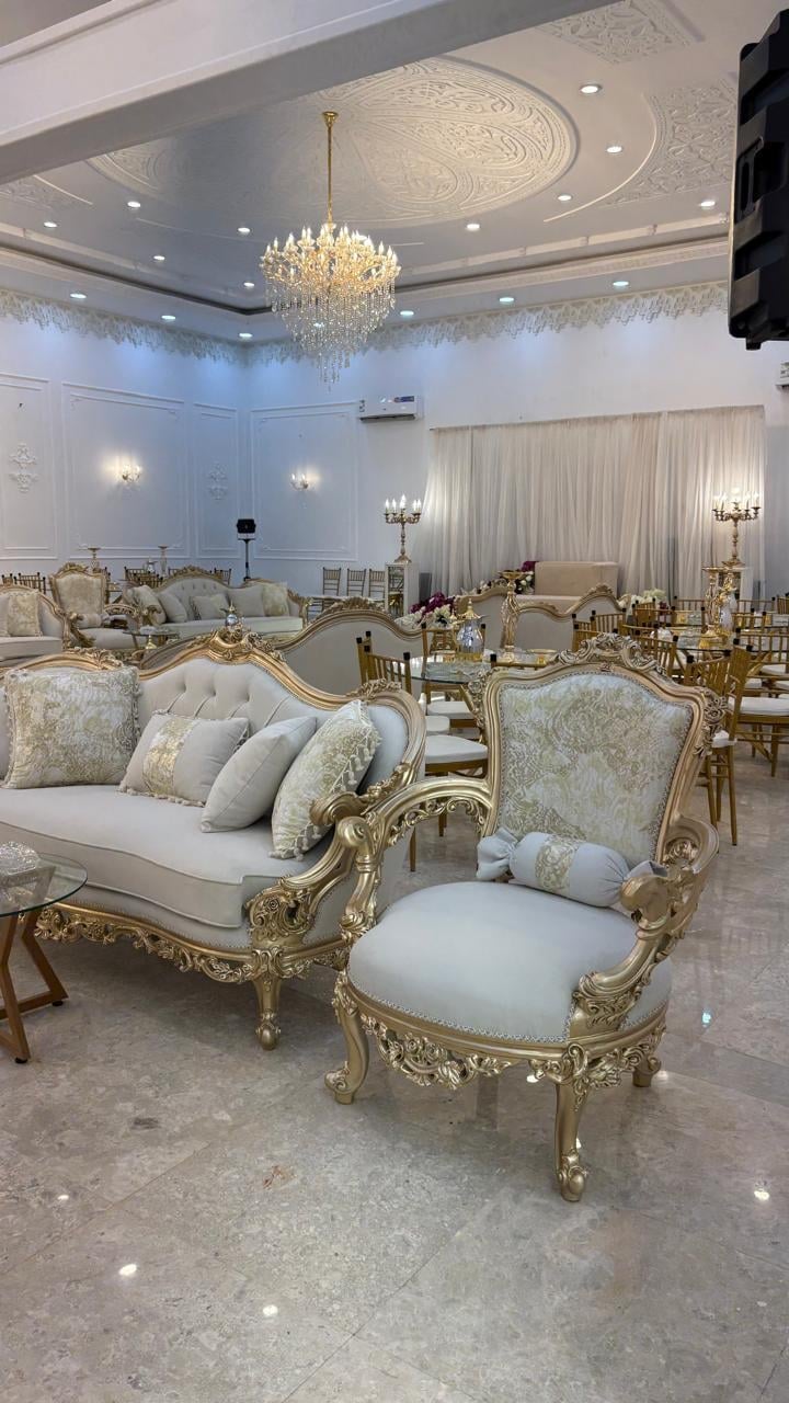 Luxurious ornate room with gold-framed furniture, cream upholstery, crystal chandelier, decorative ceiling, and elegant white drapery