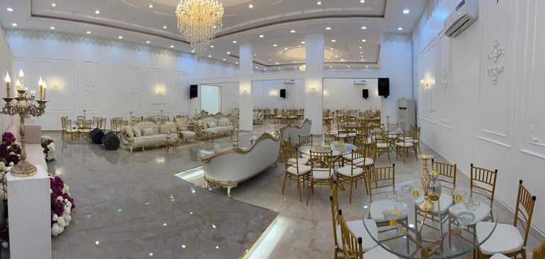 Elegant event venue with white furniture, gold chiavari chairs, crystal chandelier, and polished tile flooring